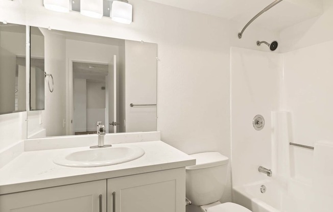 A white bathroom with a sink, toilet, and shower.
