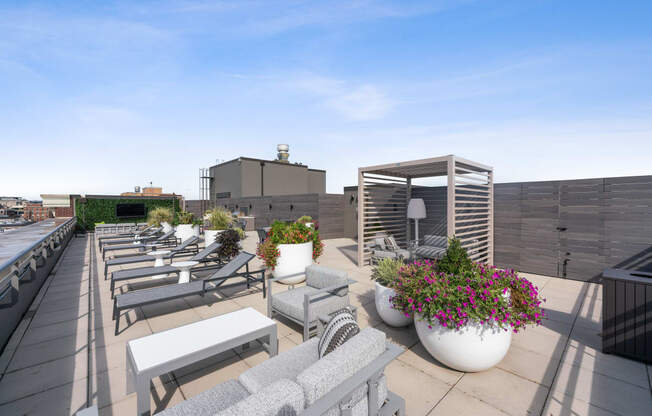a roof top patio with lounge chairs and tables and potted plants
