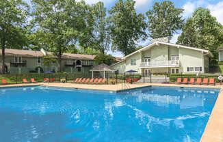 A swimming pool in front of a house with trees in the background.