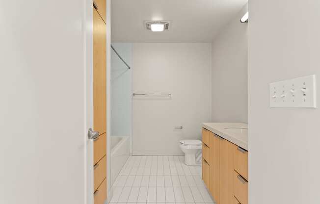 A white tiled bathroom with a toilet, sink, and shower.