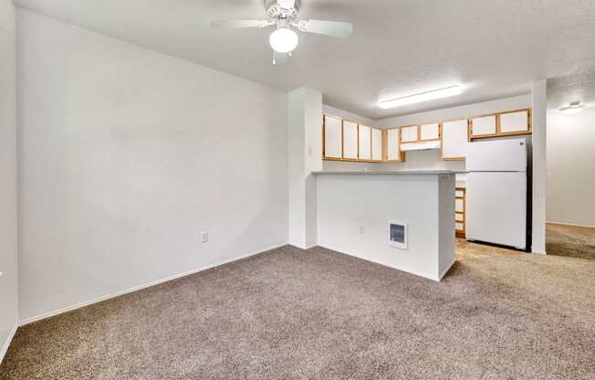 an empty living room with a kitchen and a ceiling fan