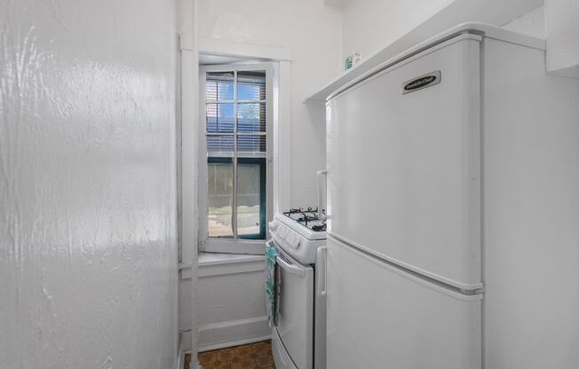 a small white kitchen with a window and a white refrigerator