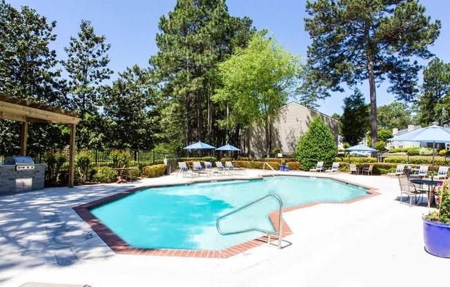 A pool surrounded by trees and chairs.