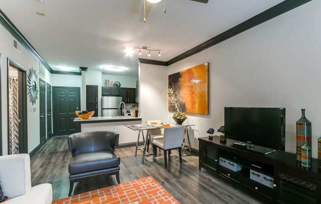 a living room with a tv and a kitchen with a table and chairs