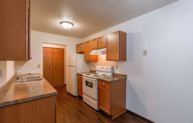 A kitchen with wooden cabinets and white appliances and a sink. Fargo, ND Long Island Apartments.