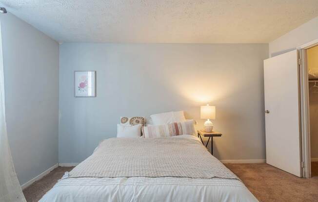 A bedroom with a bed, pillows, a nightstand, and a lamp.