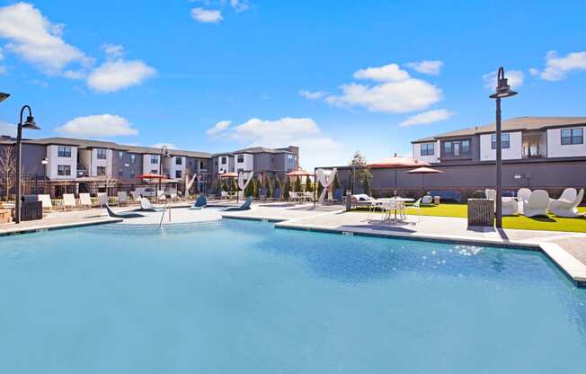 a resort style pool with lounge chairs and umbrellas with apartments in the background