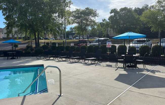 A pool area with a table and chairs and a blue umbrella.
