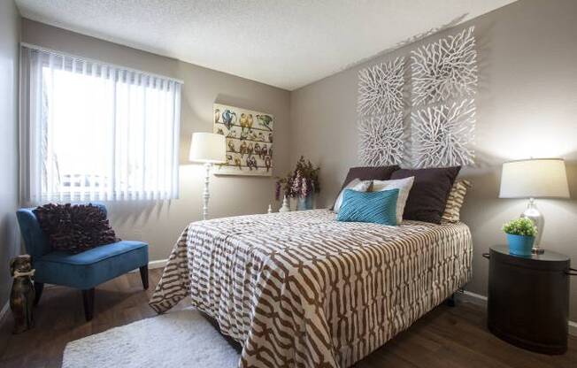 A bedroom with a patterned bedspread and a blue chair.