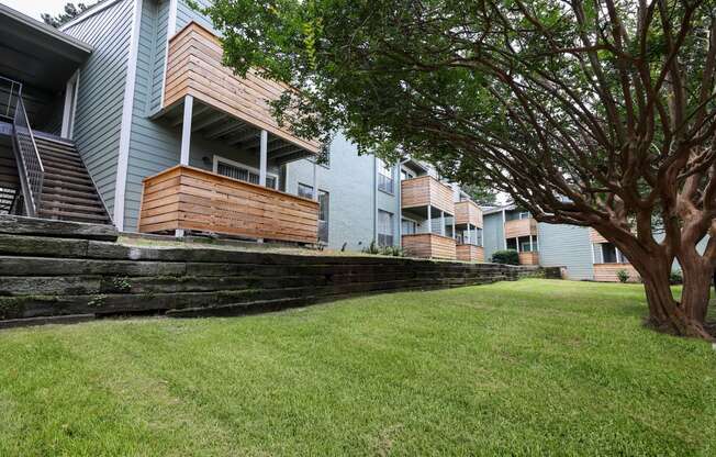 a grassy area with a tree in front of an apartment building