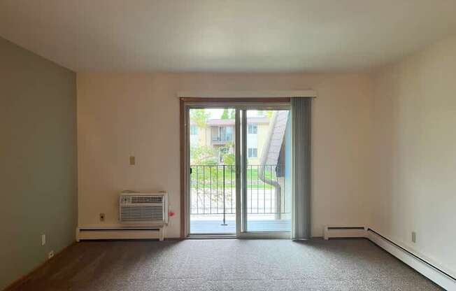 A room with a carpeted floor and a window with a view of a building outside.