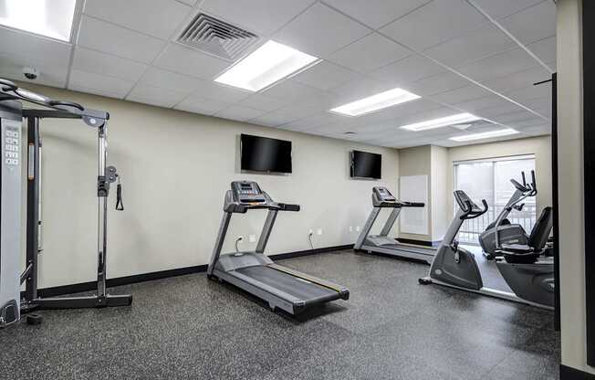 A gym with treadmills, elliptical machines, and a television.