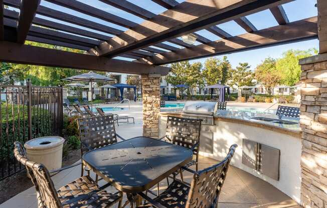 Rancho Cucamonga Apartments for Rent - Barrington Place - Poolside BBQ Area Under a Pergola, with Grill Station, Double-Sink, Table, and Chairs