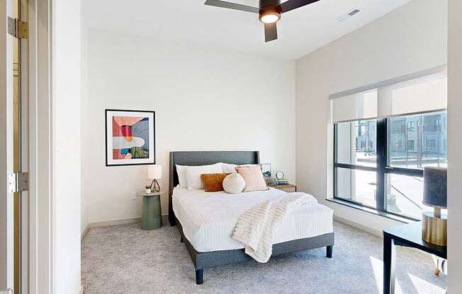 a view of the bedroom from the doorway, furnished with modern decor, a ceiling fan, and a large window overlooking the courtyard
