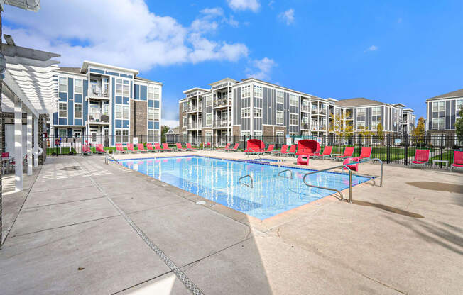 a swimming pool with red chairs and an apartment building in the background