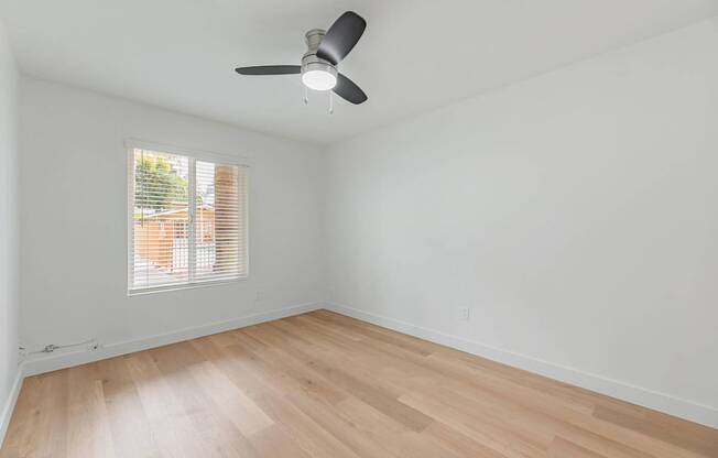 A room with a ceiling fan and a window with blinds.