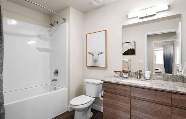 a bathroom with a white bathtub and a white toilet next to a sink with a mirror at The Flats at Riverwoods, Provo, UT, 84604
