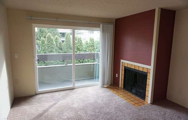 A living room with fireplace, large glass sliding door looking out onto trees at Heritage Grove, Renton, WA.