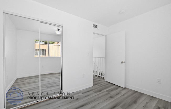 a white walled room with a mirrored door and a staircase