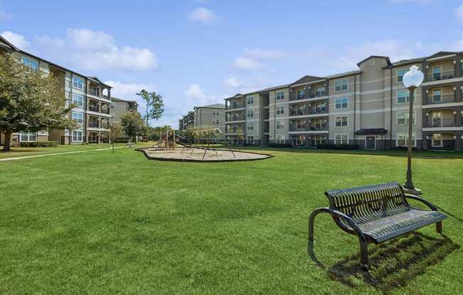 greenspace area with a park bench and playground area at Park at Magnolia apartments