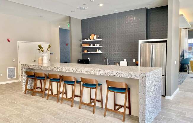 A community clubhouse kitchen with a long bar, a refrigerator, a sink, and six barstools.