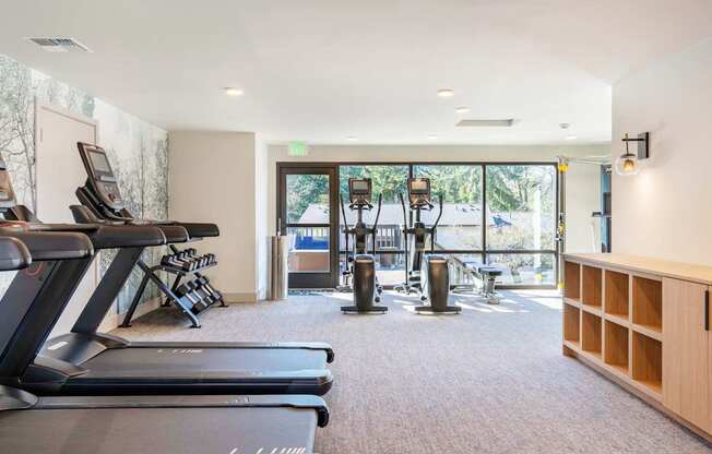 A gym with treadmills, weights, and a green exit sign.