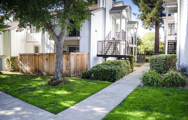 View of grassy area between two buildings, showing off private patio/balcony and side walk winding through