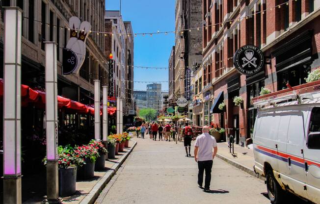 A man is walking down a street lined with potted plants and shops.