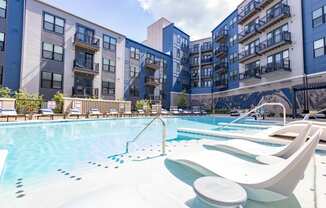 an outdoor swimming pool with chaise lounge chairs and an apartment building in the background