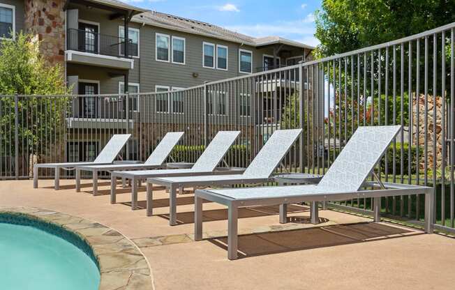 a row of chaise lounges next to a pool with an apartment building in the