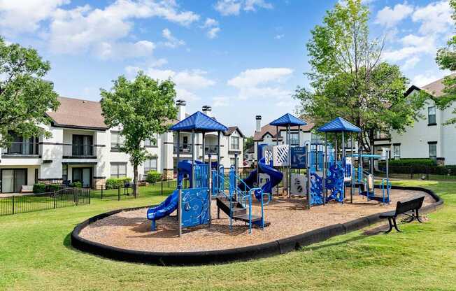 Community playground with blue climbing structures and slides set on a grassy lawn.