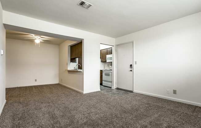 an empty living room with carpet and a door to a kitchen