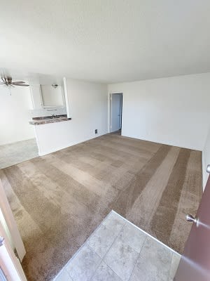 an empty living room with a kitchen in the background