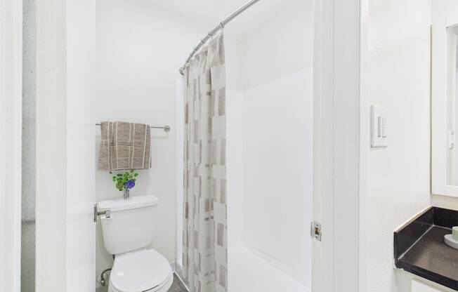 A white toilet with a towel on the roll and a shower curtain.