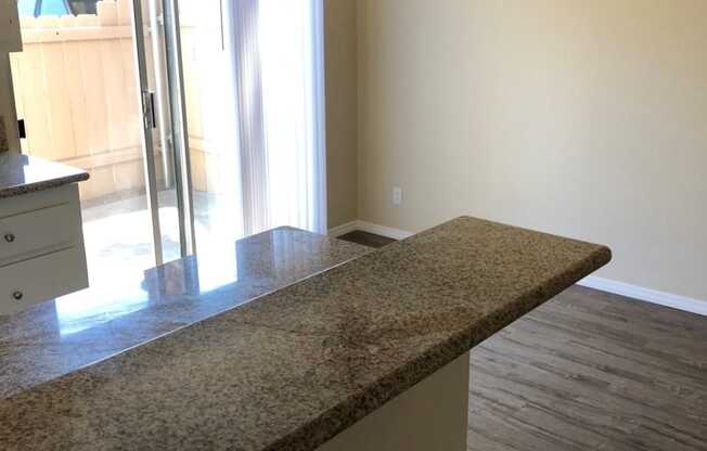 View of kitchen serving bar and dining area with sliding glass door to private porch at Plaza Verde Apartments in Escondido, California.