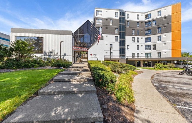 a sidewalk in front of a building with a flag at Troy Place Apartments - Troy, MI, Troy, Michigan