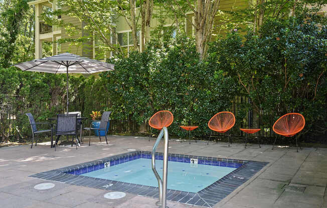 A pool surrounded by orange chairs and a green hedge.