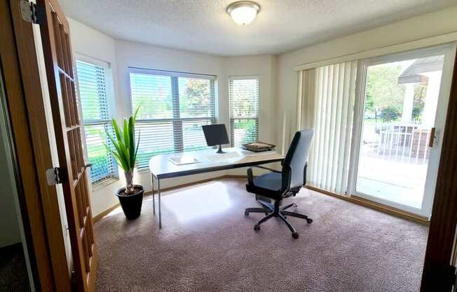 A room with a desk, chair, and potted plant.