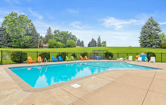 A large outdoor swimming pool surrounded by a fence and lounge chairs.