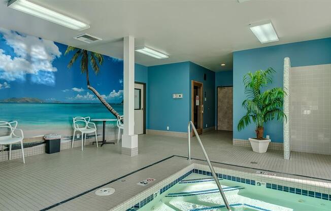 Apartments for Rent in Spokane, WA - Canyon Bluffs - Indoor Pool with Tiled Flooring, White Table with Chairs, Potted Plant, and Wall Mural of Beach Scenery.