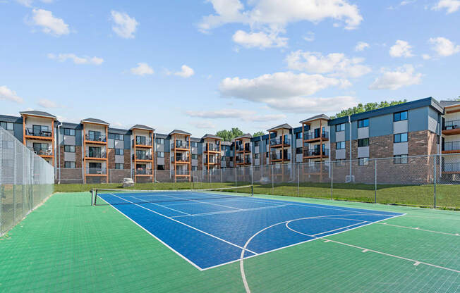 A tennis court is surrounded by a chain link fence and apartment buildings.