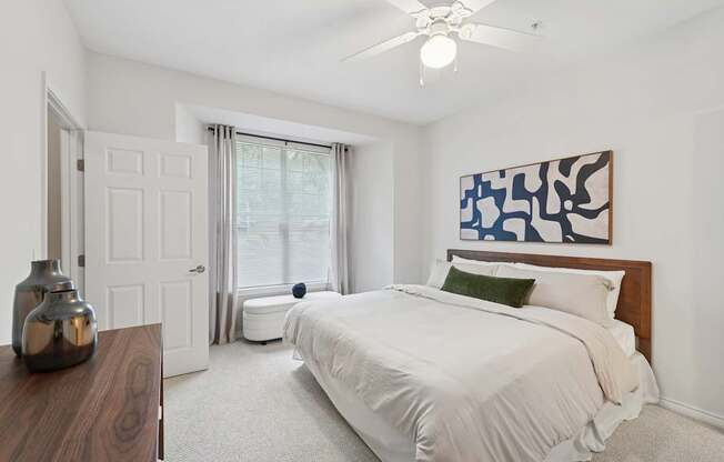 A bedroom with a bed, a ceiling fan, and a painting on the wall.
