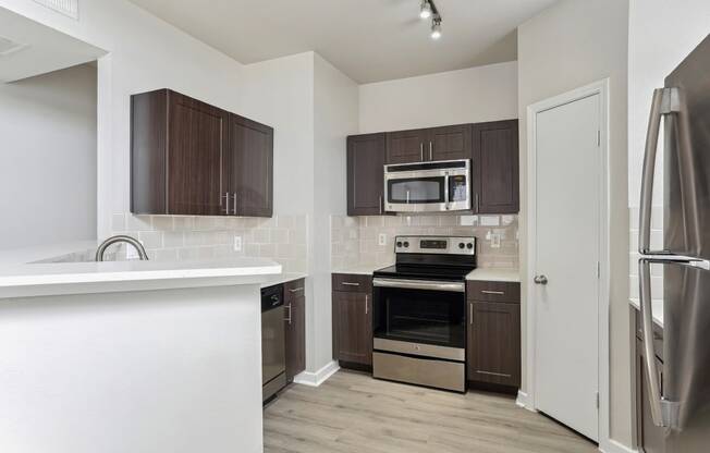 Modern kitchen with stainless steel appliances, quartz countertops, designer tile backsplash, custom cabinetry, and wood-style flooring