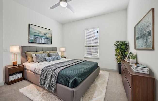 A bedroom with a bed, nightstand, and a plant.