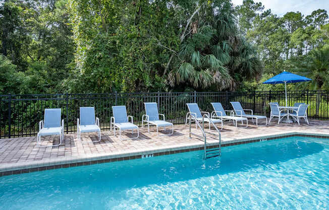 A pool surrounded by trees and chairs.