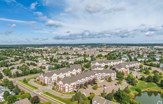 A large apartment complex with a pond in the foreground and a cloudy sky above.