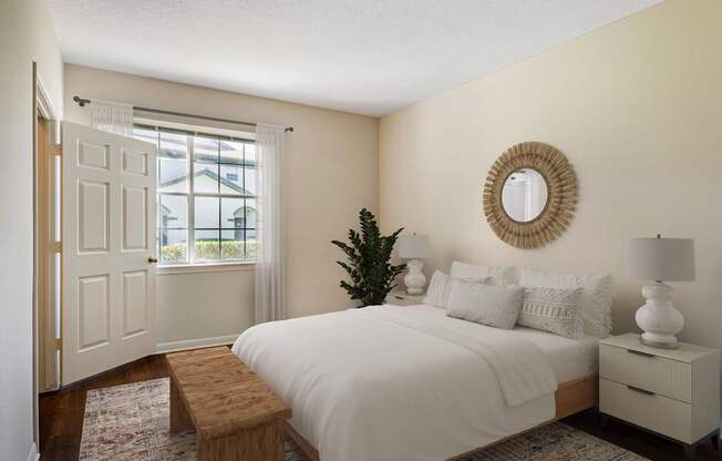 A bedroom with a white bed, a wooden bench, and a round mirror on the wall.