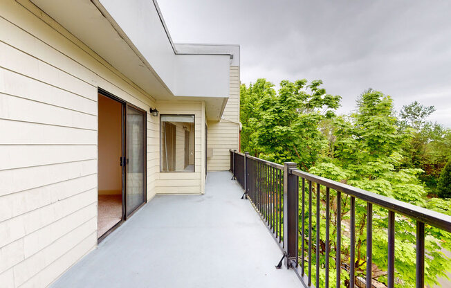 A spacious private balcony here at Heritage Hills featuring a smooth concrete floor, black metal railing, and direct access from sliding glass doors. The balcony overlooks mature trees and greenery, providing a peaceful outdoor setting with ample room for seating or relaxing while enjoying natural views and fresh air.