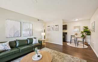 A living room with a green couch, a coffee table, and a dining area in the background.