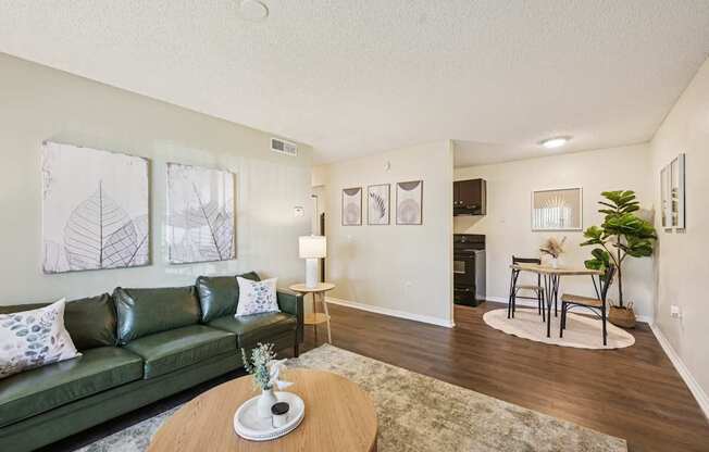 A living room with a green couch, a coffee table, and a dining area in the background.